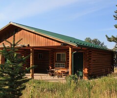 A log cabin with a green roof, a porch with chairs, and a door marked with the number 3.