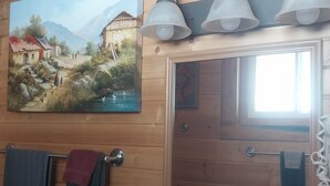 A wooden cabin interior with a painting of a rural scene, a door with a towel rack, and a window. - Liberty Belle Lodge (Aladdin)