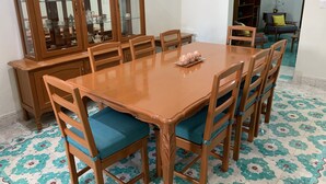 Un comedor con una mesa y sillas de madera, un aparador de vidrio con vajilla, y un piso con diseño.
