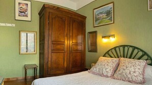 Quarto com guarda-roupa de madeira grande, cama com almofadas florais e duas fotografias emolduradas na parede.