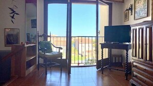 Varanda ampla com porta de correr, televisão sobre suporte e uma cadeira.