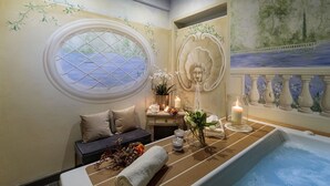 Um quarto de spa com banheira, janela com vista, parede decorativa e uma pequena mesa com velas e flores.