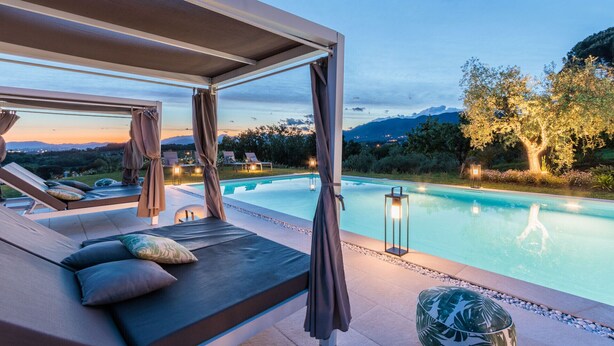 A poolside lounge area with a view of mountains and trees at dusk.