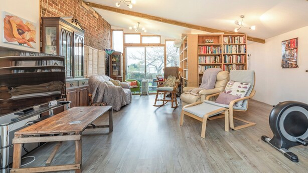A cozy living room with a fireplace, bookshelves, a dining table, and a treadmill. - Sheepwash Square House (Sheepwash, near Beaworthy)