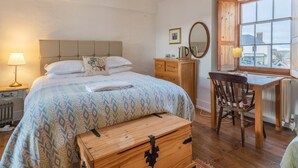 A bedroom with a bed, bedside table, dresser, desk, chair, and a window with a view. - Sheepwash Square House (Sheepwash, near Beaworthy)