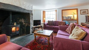 A cozy living room with a stone fireplace, a comfortable sofa set, a television, and a bookshelf. - Sheepwash Square House (Sheepwash, near Beaworthy)