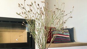 A rustic wooden vase with dried plants on a round table, a small glass candle holder, and a woven basket in a cozy room with a striped pillow and a framed picture on the wall. - Trendy villa with a remarkable view. (Santa Bárbara de Nexe)