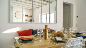 A dining area with a wooden table set for four, including plates, cutlery, and wine glasses. A large mirror reflects the room, and a window provides natural light. - Trendy villa with a remarkable view. (Santa Bárbara de Nexe)