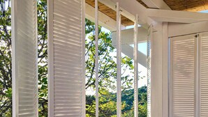 A covered porch with white shutters, a wooden bench, and a variety of cushions. - Trendy villa with a remarkable view. (Santa Bárbara de Nexe)