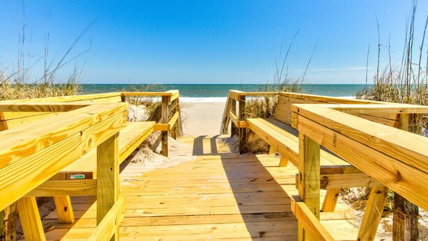 A wooden boardwalk leading to a beach with clear skies.