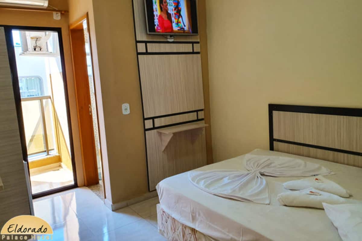 A hotel room with a bed, a television mounted on the wall, and a window with curtains.