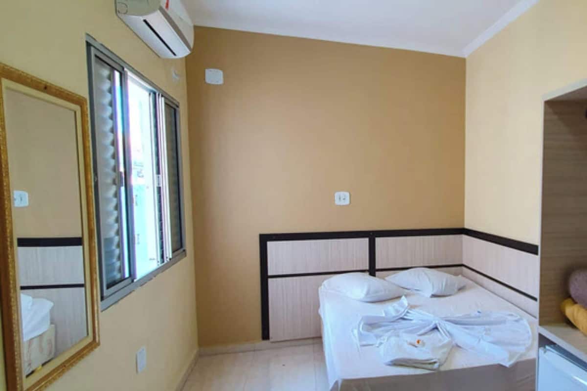 A bedroom with a bed, a window, an air conditioner, and a wardrobe.