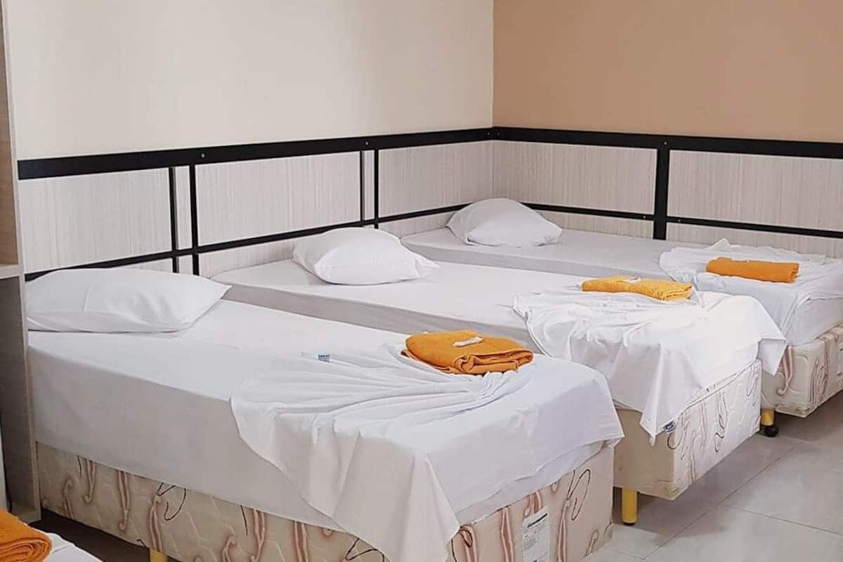 A hotel room with three single beds, each with white bedding and pillows.
