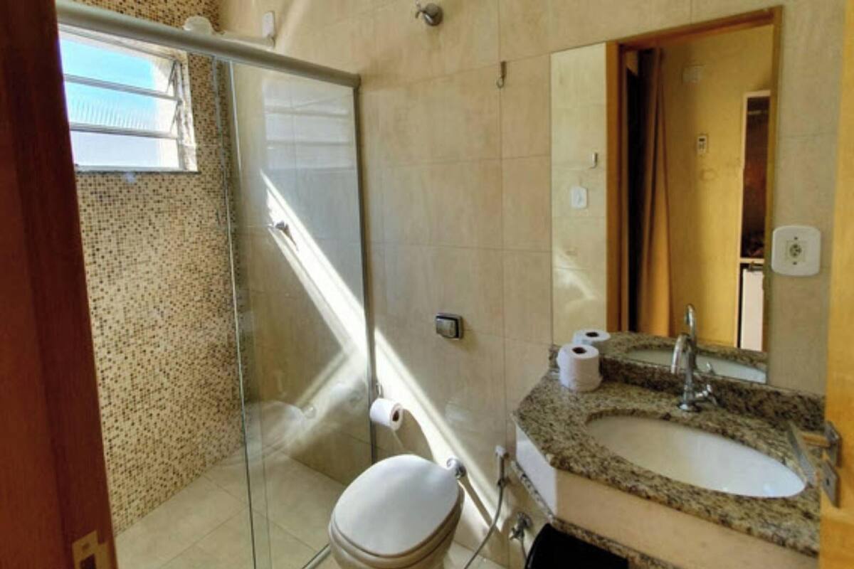 A bathroom with a glass shower enclosure, a toilet, a sink with a granite countertop, and a mirror.