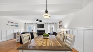 Ein Esszimmer mit Holztisch, weißen Stühlen, einem Deckenventilator und einer Zierpflanze.