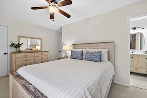 A bedroom with a wooden bed, a ceiling fan, a nightstand with a lamp, a dresser, and a mirror.