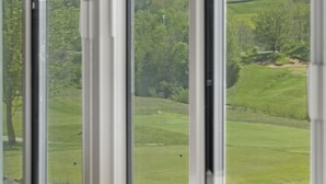 Une vue sur un terrain de golf, prise à travers une fenêtre équipée de stores verticaux.