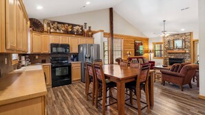 A spacious kitchen with wooden cabinets, a dining table with chairs, and a fireplace in the living area. - Lovely Cabin in the Heart of Branson! Gas Fireplace & Jetted Tub, Ticket/Golf Discounts (Branson)