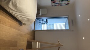 Une chambre à coucher avec un lit, un plancher en bois, une fenêtre et un luminaire au plafond.