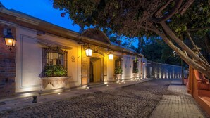 Un edificio histórico con calle adoquinada, entrada iluminada y plantas en macetas.