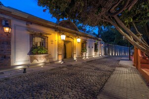 Un edificio histórico con calle adoquinada, entrada iluminada y plantas en macetas.