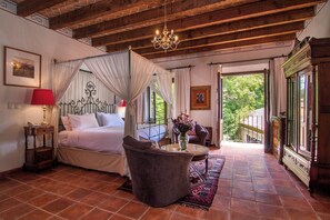 A bedroom with a four-poster bed, a sitting area with a coffee table, and a view of the outdoors. - Villa Santa Monica (San Miguel de Allende)