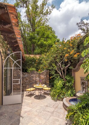 An outdoor patio with a stone wall, a table with chairs, and a fountain. - Villa Santa Monica (San Miguel de Allende)