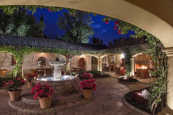 Un patio con una fuente, plantas en macetas y mobiliario exterior.