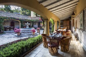An outdoor patio with stone flooring, wooden tables and chairs, a fountain, and potted plants. - Villa Santa Monica (San Miguel de Allende)