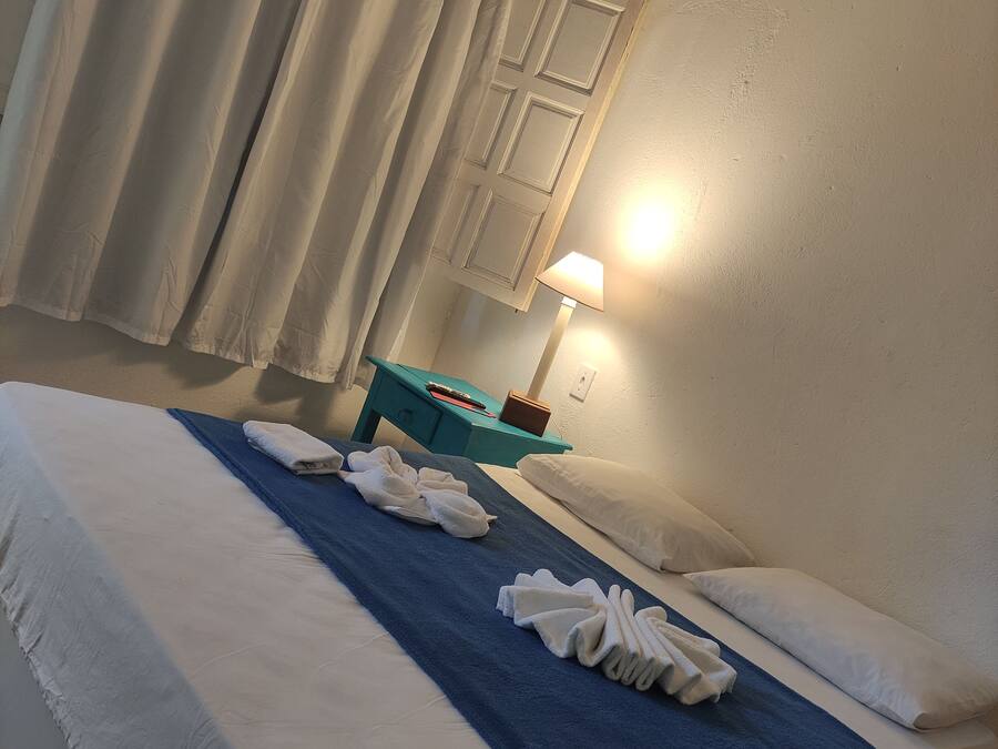 Ett hotellrum med en säng, ett skrivbord, en lampa och ett fönster med gardiner.