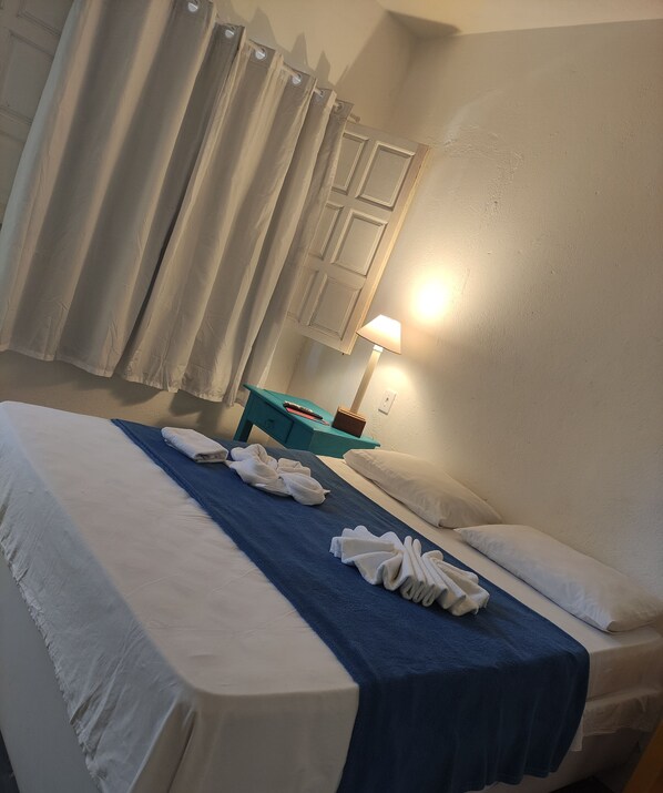 Quarto de hotel com cama, escrivaninha, luminária e janela com cortinas.