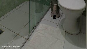 A bathroom with a glass shower enclosure, a toilet, and a window with a curtain.