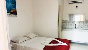 A single bed with white and red bedding, a small bedside table, and a wall-mounted air conditioner.