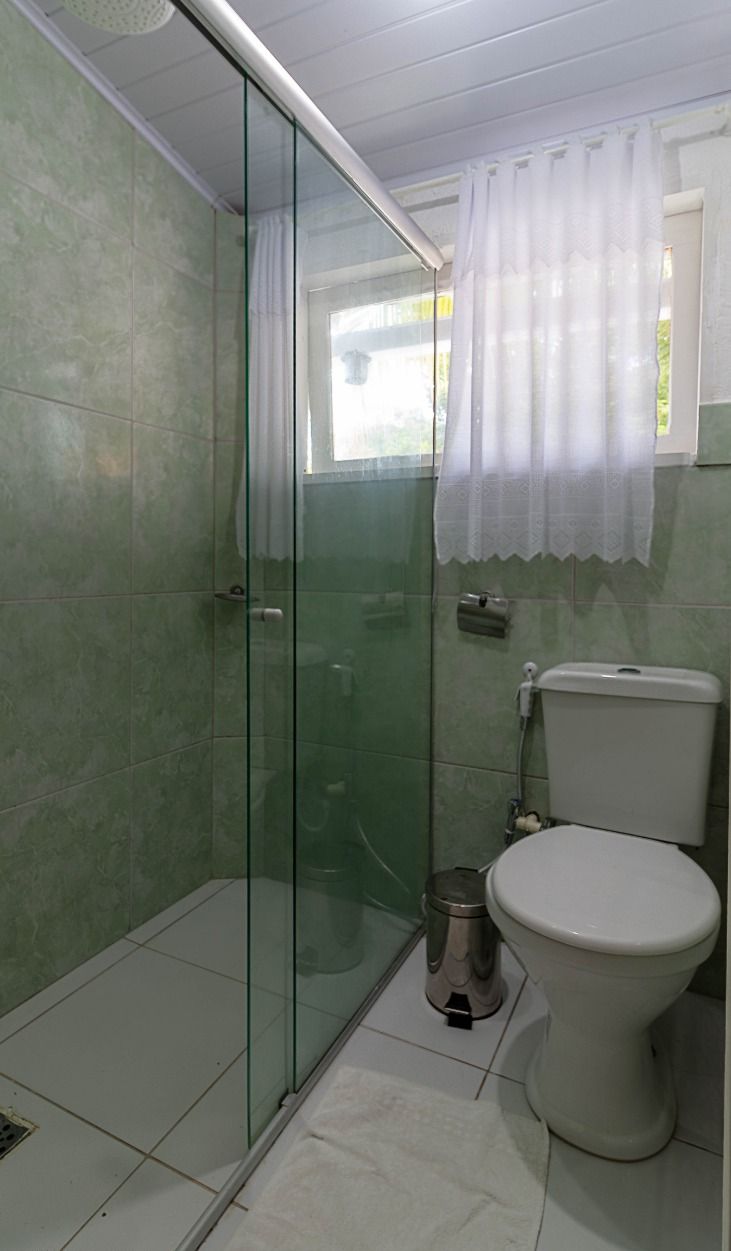 Un baño con cabina de ducha de vidrio, inodoro y ventana con cortina.