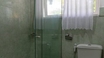 Un baño con cabina de ducha de vidrio, inodoro y ventana con cortina.