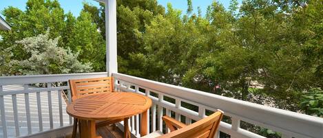 Une terrasse en bois avec une table ronde et des chaises, entourée de rampes blanches, offrant une vue sur un paysage verdoyant et luxuriant.