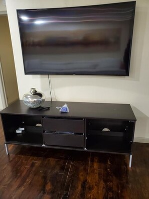 A flat-screen TV mounted on a wall above a dark wooden entertainment center with drawers and a decorative bowl. - Buckhead 5BDR Home 7Queenbeds 6Tvs Sleep15pple Near LenoxMall WiFi Patio Garden (Atlanta)