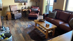 Ein Wohnzimmer mit einem braunen Ledersofa, einem Holztisch, einem gerahmten Bild eines Elchs und einem Schild mit der Aufschrift "Welcome to the Mountain".
