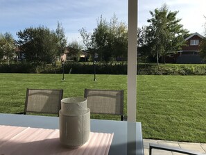 Un área de estar al aire libre con una mesa y sillas, un jarrón decorativo y vistas a un césped cuidado y árboles.