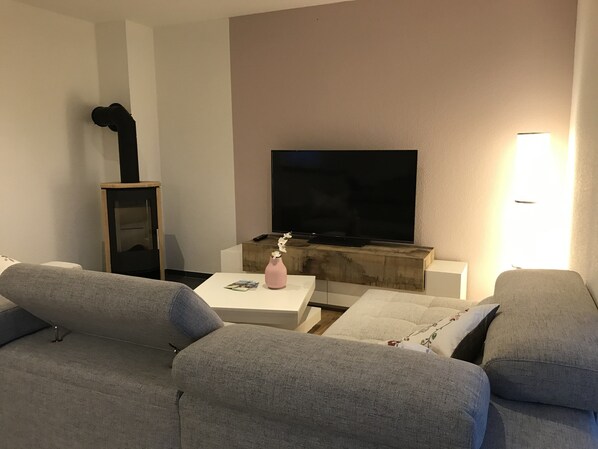 Una sala de estar moderna con un televisor de pantalla plana, sofás grises, una mesa de centro blanca y un jarrón rosa.
