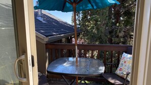 Un patio con una mesa metálica redonda y una sombrilla azul, rodeado de sillas de mimbre y una terraza de madera.