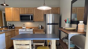 Una cocina moderna con armarios de madera, electrodomésticos de acero inoxidable, una isla central con taburetes y una lámpara colgante.