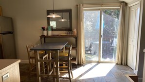 Una cocina con una mesa de comedor, sillas, un refrigerador, un lavaplatos y una ventana con cortinas.