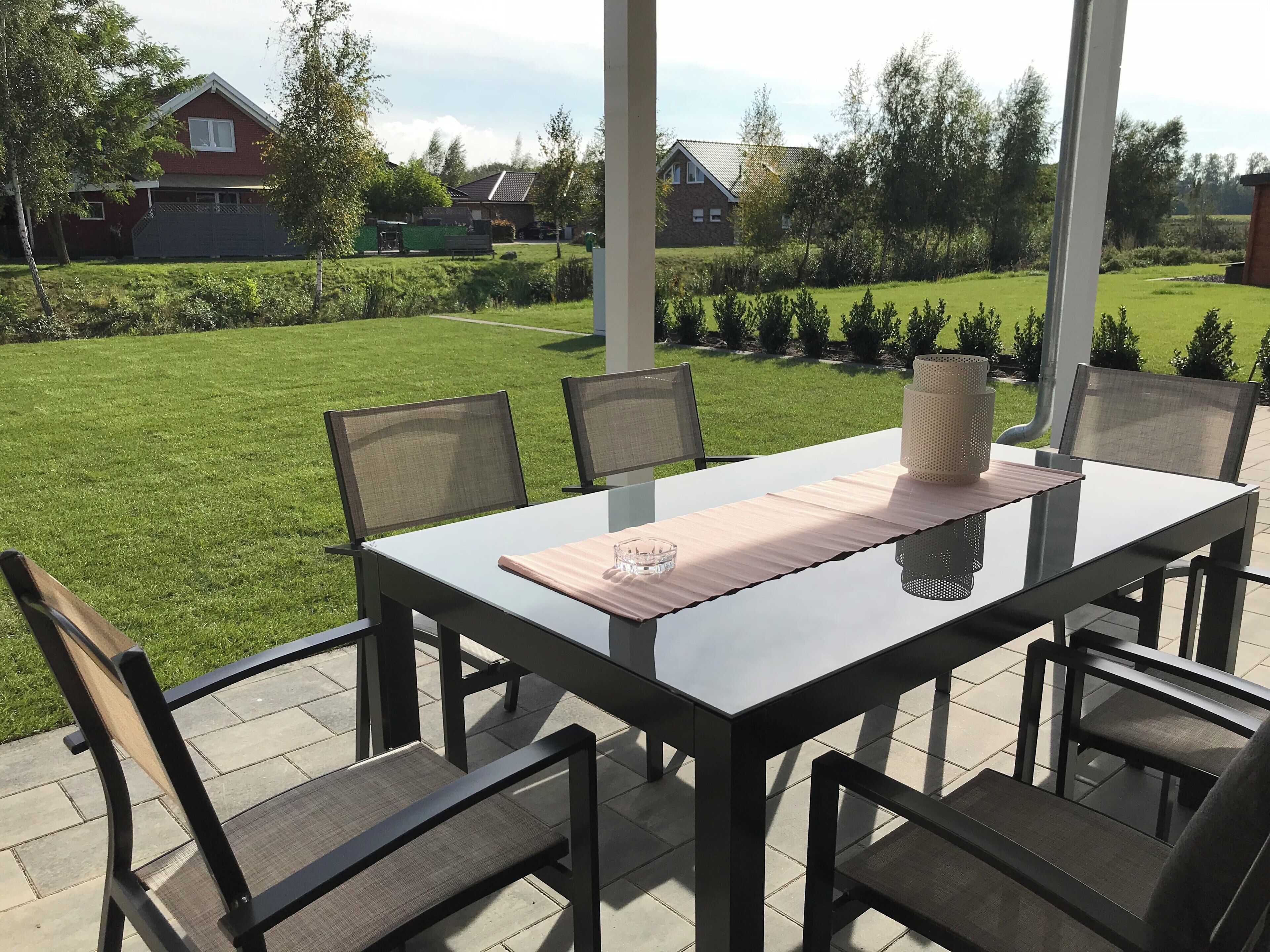 An outdoor patio with a glass-top table, four chairs, and a decorative vase.