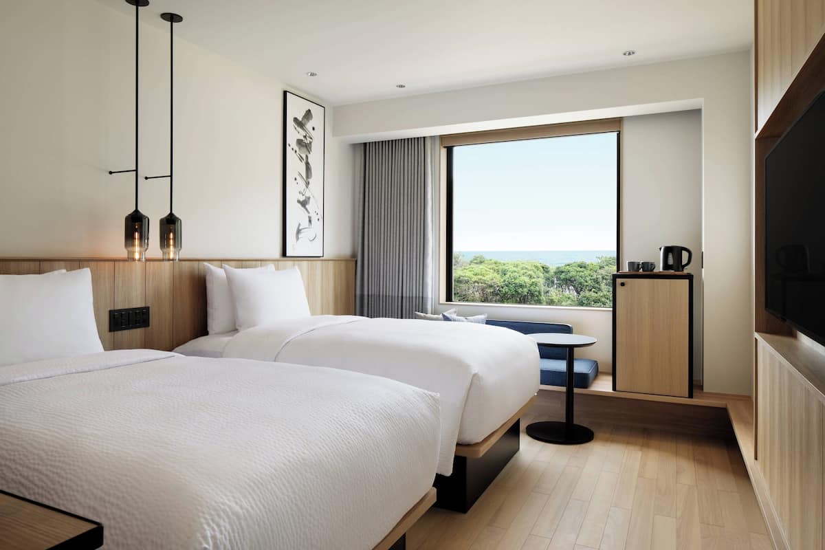 Een moderne hotelkamer met twee bedden, een groot raam met uitzicht, een klein tafeltje en een televisie.