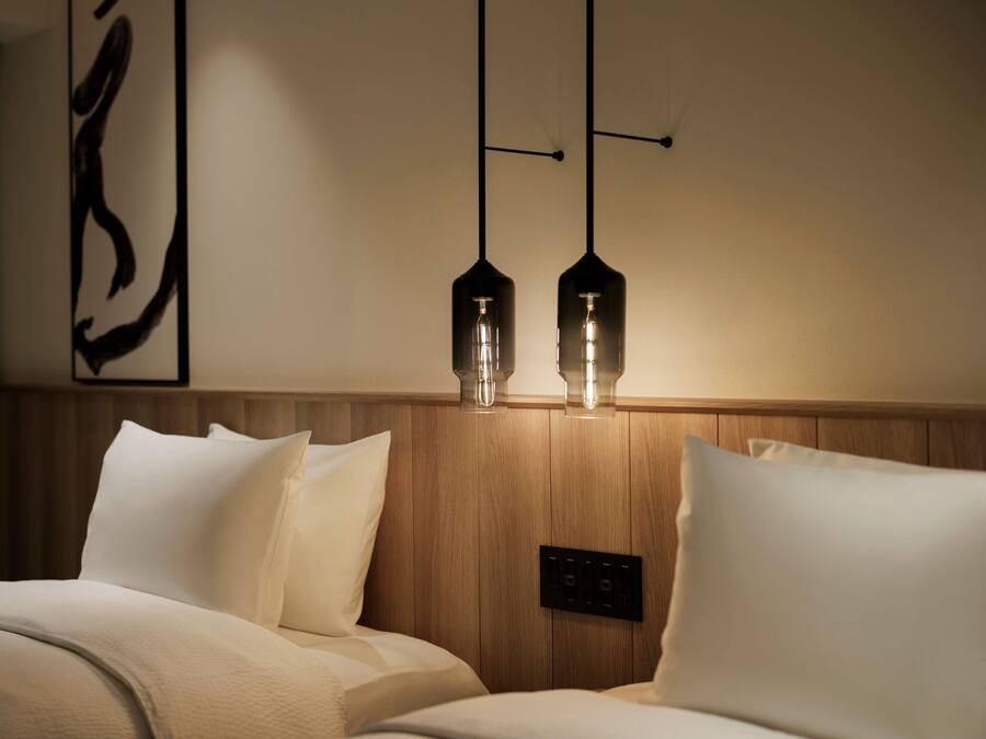A hotel room with a wooden headboard, two bedside lamps, and a wall-mounted control panel.