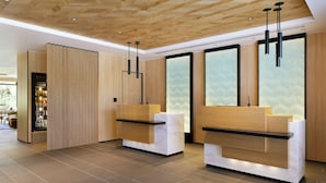 Un espace d’accueil moderne, doté de comptoirs de réception en bois, d’un grand mur de verre et d’un plafond orné de panneaux de bois.