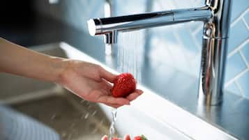 A hand holding a strawberry under a running tap in a kitchen sink.