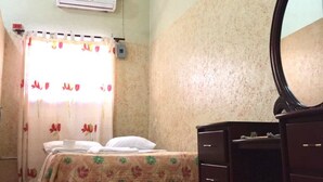 A bedroom with a bed, a dresser, a mirror, an air conditioner, and a window with floral curtains. - Hotel Verano Azul (Santo Domingo)