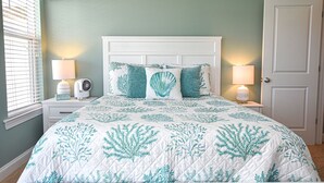 A bedroom with a bed, two bedside lamps, a nightstand, a door, and a window with blinds. - Enjoy Belle of the Beach -  Your Family Get Away!  **Linens Included** (Carolina Beach)